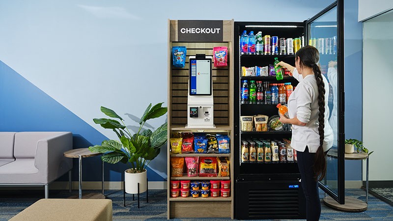 Open snack shelves and a self-checkout kiosk beside a stocked cooler.